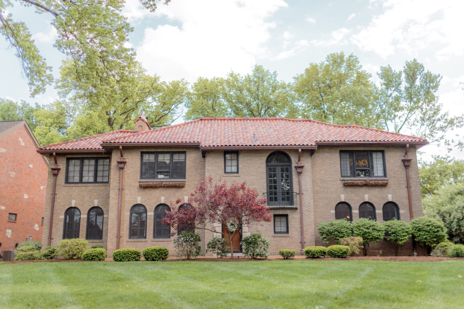 Elegant brick house with red roof and lush green lawn.