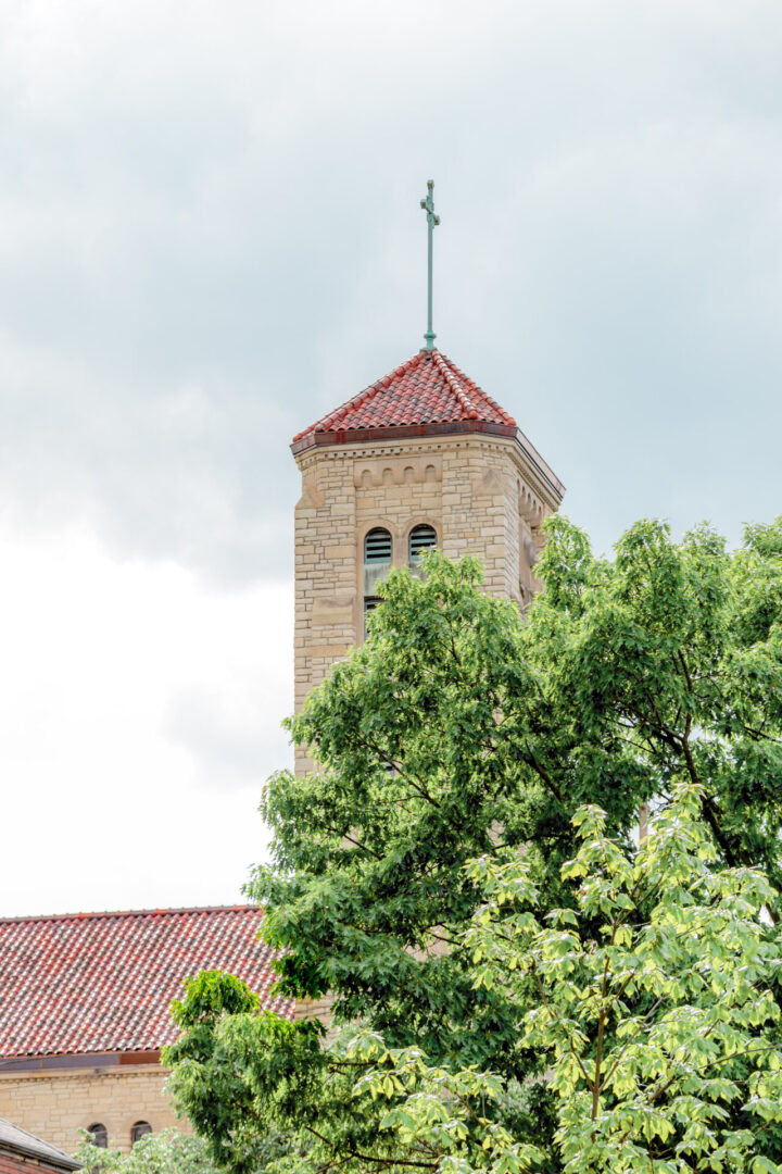 A stone bell tower with a red roof behind green trees.