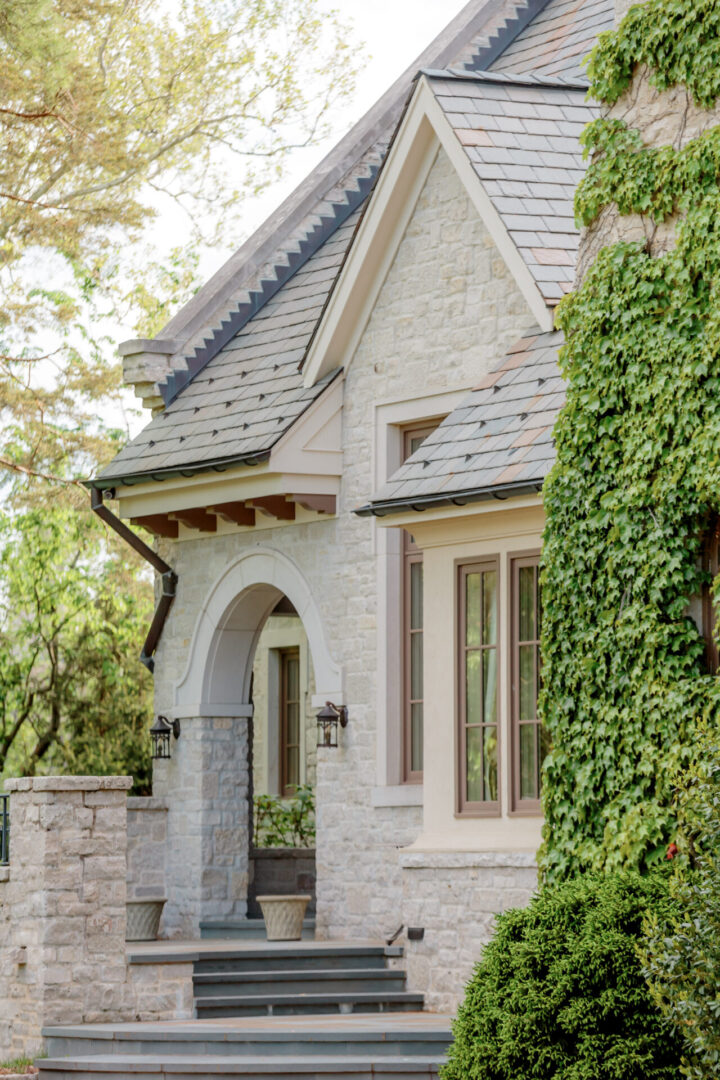 Charming stone house entrance with archway and lush greenery.