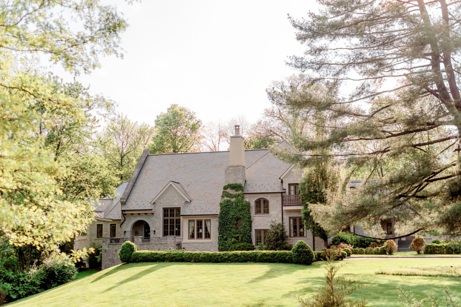 Elegant stone house with a steep roof and lush green lawn.