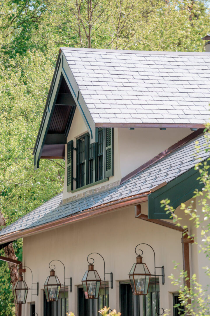 Close-up of a house roof with a dormer window surrounded by greenery.