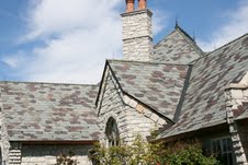 Stone house with a steep slate roof and chimney under a blue sky.