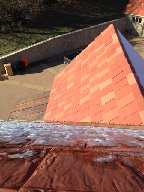Close-up of a rooftop with reddish-orange shingles and a copper flashing.